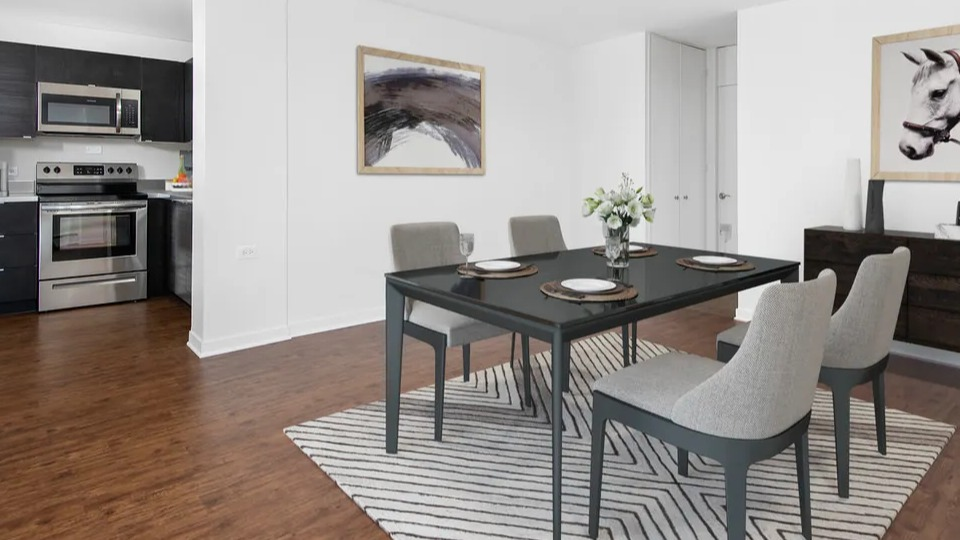 Open dining area with four modern chairs, a black table, and a patterned rug set beside the kitchen at 55 West Chestnut apartments in Chicago, great for entertaining
