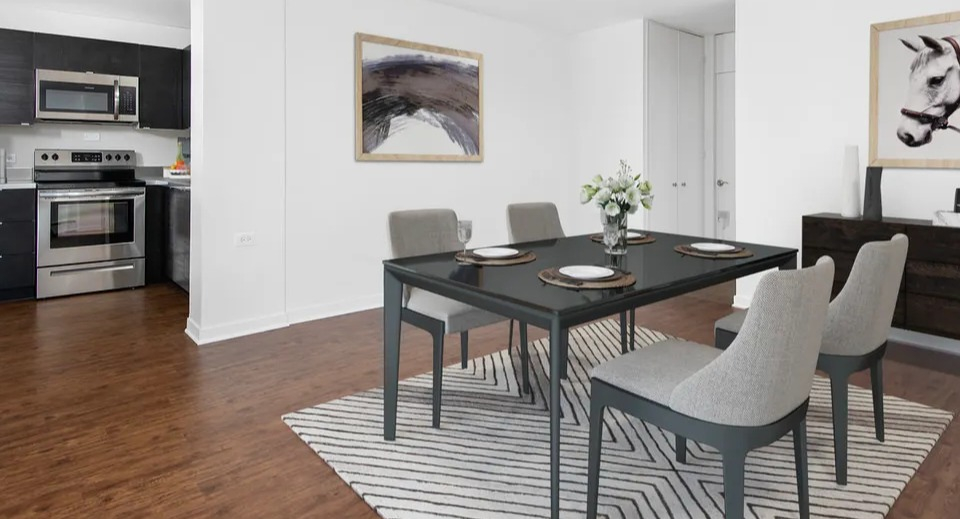 Open dining area with four modern chairs, a black table, and a patterned rug set beside the kitchen at 55 West Chestnut apartments in Chicago, great for entertaining
