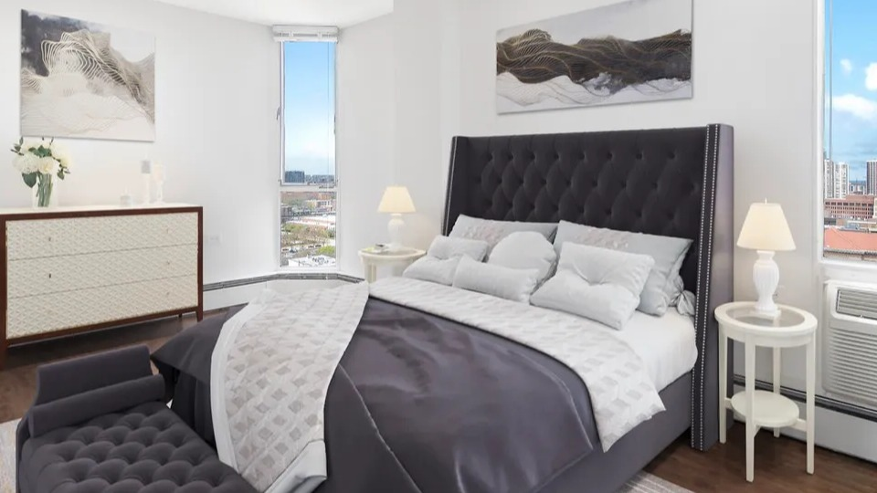 Stylish bedroom with tufted headboard, upholstered bench, bedside tables, and two tall windows bringing skyline views at 55 West Chestnut apartments in Chicago