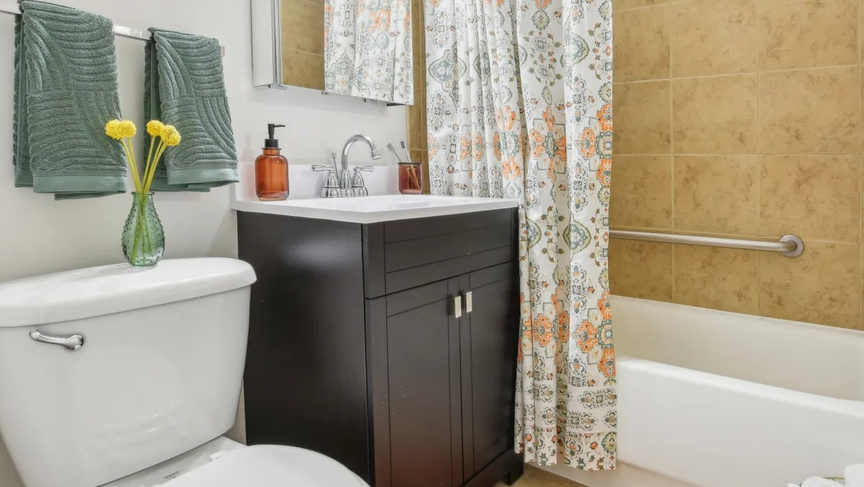 Updated bathroom with tan tile tub-shower, dark vanity, bright lighting, and patterned curtain at 55 West Chestnut apartments in Chicago