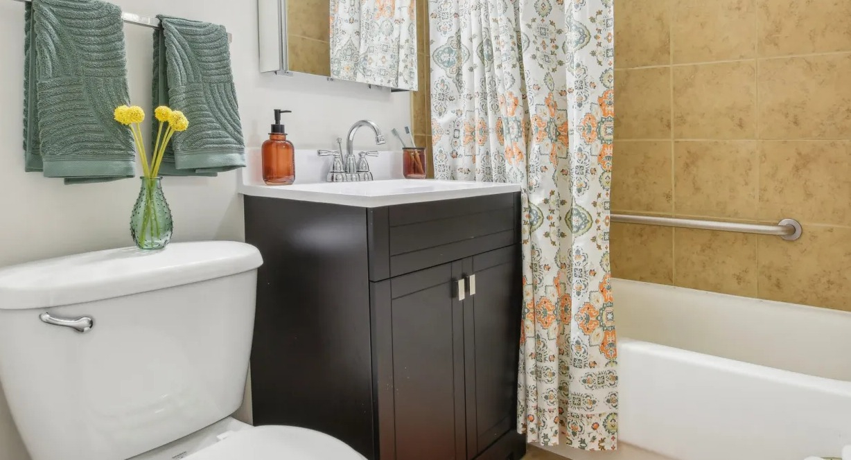Updated bathroom with tan tile tub-shower, dark vanity, bright lighting, and patterned curtain at 55 West Chestnut apartments in Chicago