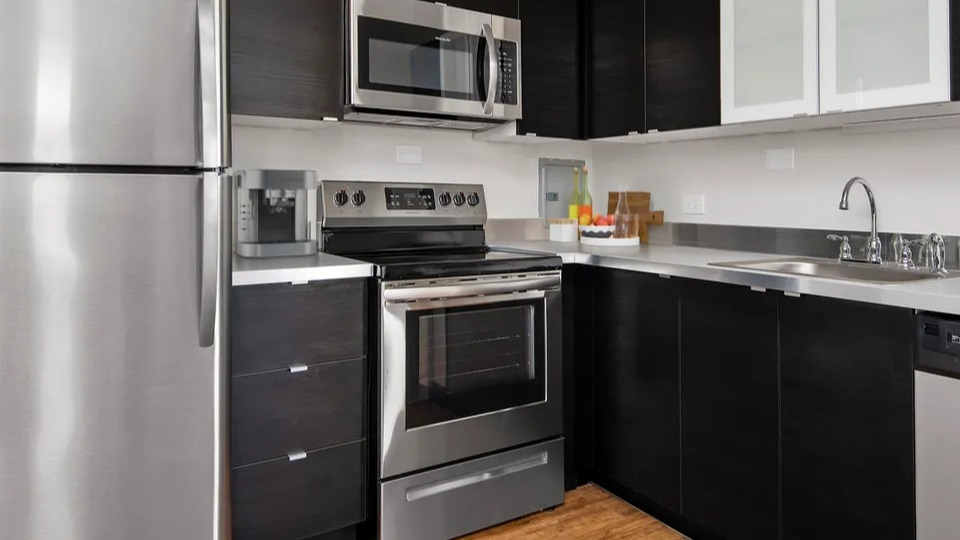 Updated kitchen with dark cabinets, stainless steel appliances, generous counter space, and wood-style flooring at 55 West Chestnut apartments in Chicago