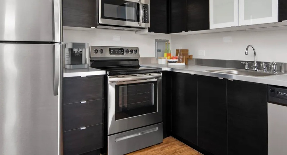 Updated kitchen with dark cabinets, stainless steel appliances, generous counter space, and wood-style flooring at 55 West Chestnut apartments in Chicago