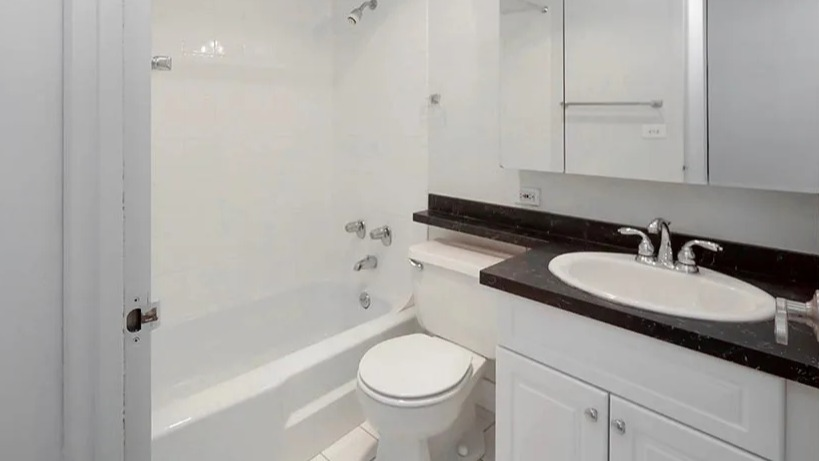 Modern bathroom with white vanity, black stone countertop, mirrored cabinets, and a tub-shower combo at 65 East Scott apartments in Chicago