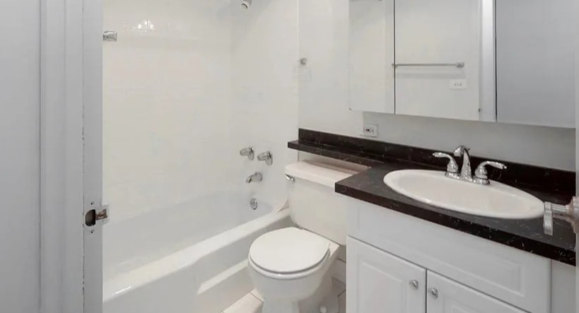 Modern bathroom with white vanity, black stone countertop, mirrored cabinets, and a tub-shower combo at 65 East Scott apartments in Chicago
