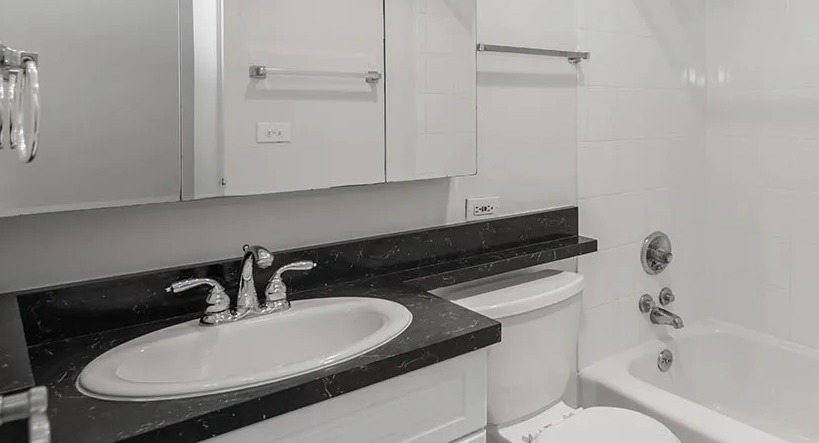 Bright modern bathroom with mirrored medicine cabinets, black stone vanity, and tub with shower at 65 East Scott apartments in Chicago
