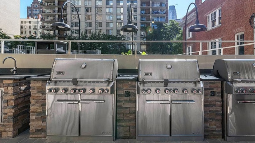 Rooftop grilling area with stainless steel Weber grills, prep counters, and city views at 65 East Scott apartments in Chicago