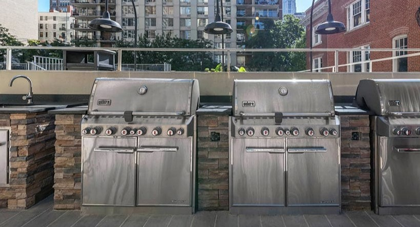 Rooftop grilling area with stainless steel Weber grills, prep counters, and city views at 65 East Scott apartments in Chicago