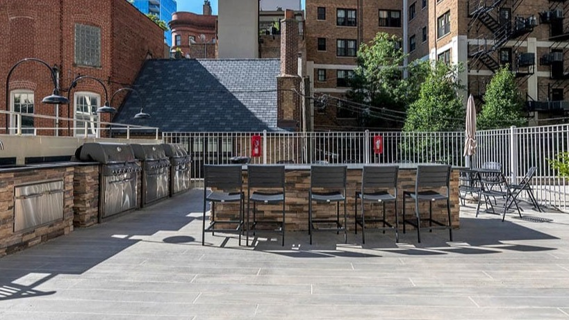 Sunny resident sundeck with built-in grill stations, bar seating, and a city backdrop at 65 East Scott apartments in Chicago