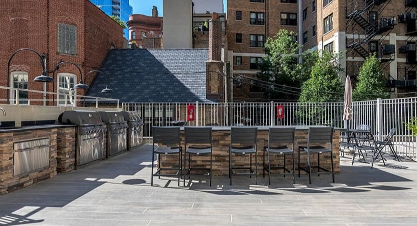 Sunny resident sundeck with built-in grill stations, bar seating, and a city backdrop at 65 East Scott apartments in Chicago