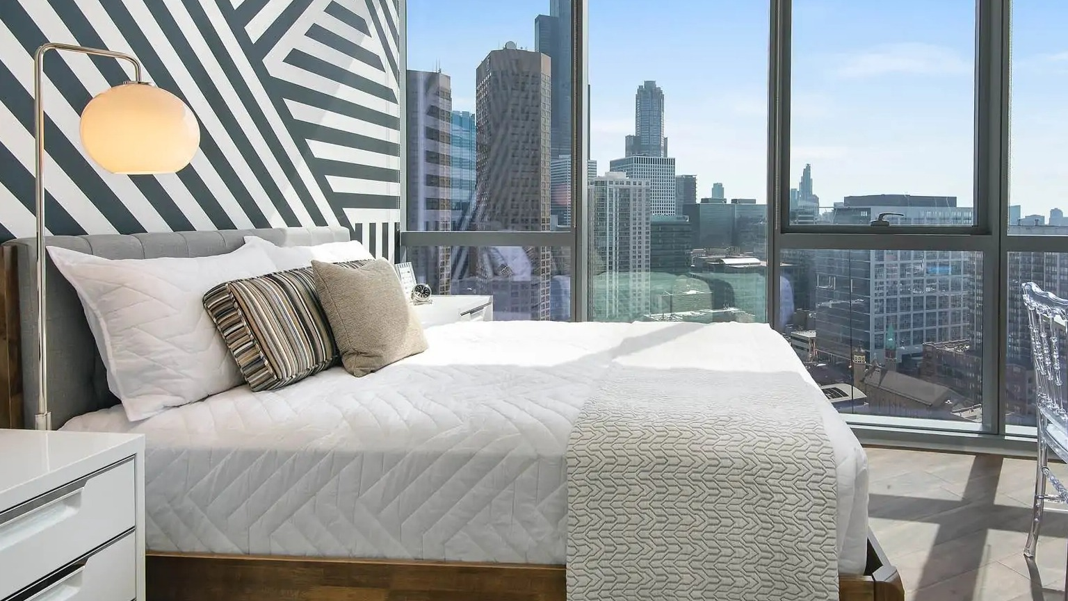 Sunlit bedroom at 727 West Madison in Chicago with bold accent wall, floor-to-ceiling windows, and sweeping skyline views