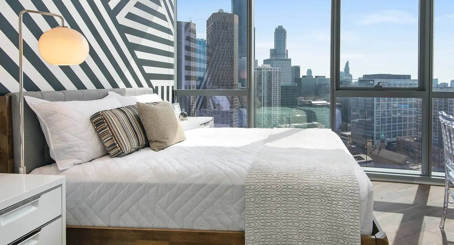 Sunlit bedroom at 727 West Madison in Chicago with bold accent wall, floor-to-ceiling windows, and sweeping skyline views