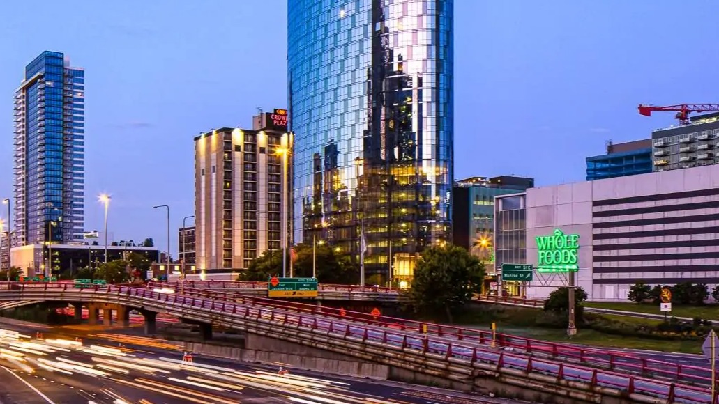 Curved glass tower of 727 West Madison rising above the West Loop at dusk, with city lights and highway motion trails in Chicago