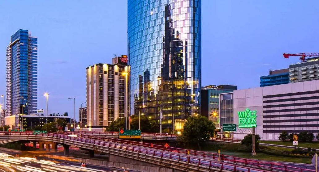 Curved glass tower of 727 West Madison rising above the West Loop at dusk, with city lights and highway motion trails in Chicago