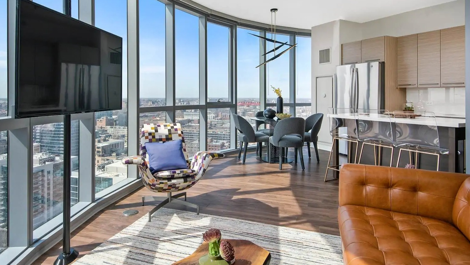 Corner living room at 727 West Madison in Chicago showcasing curved window walls, dining area, and open kitchen with dramatic city views