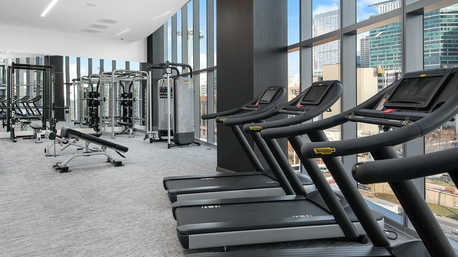 Light-filled fitness center at 727 West Madison in Chicago, with treadmills, strength equipment, and skyline views through tall windows