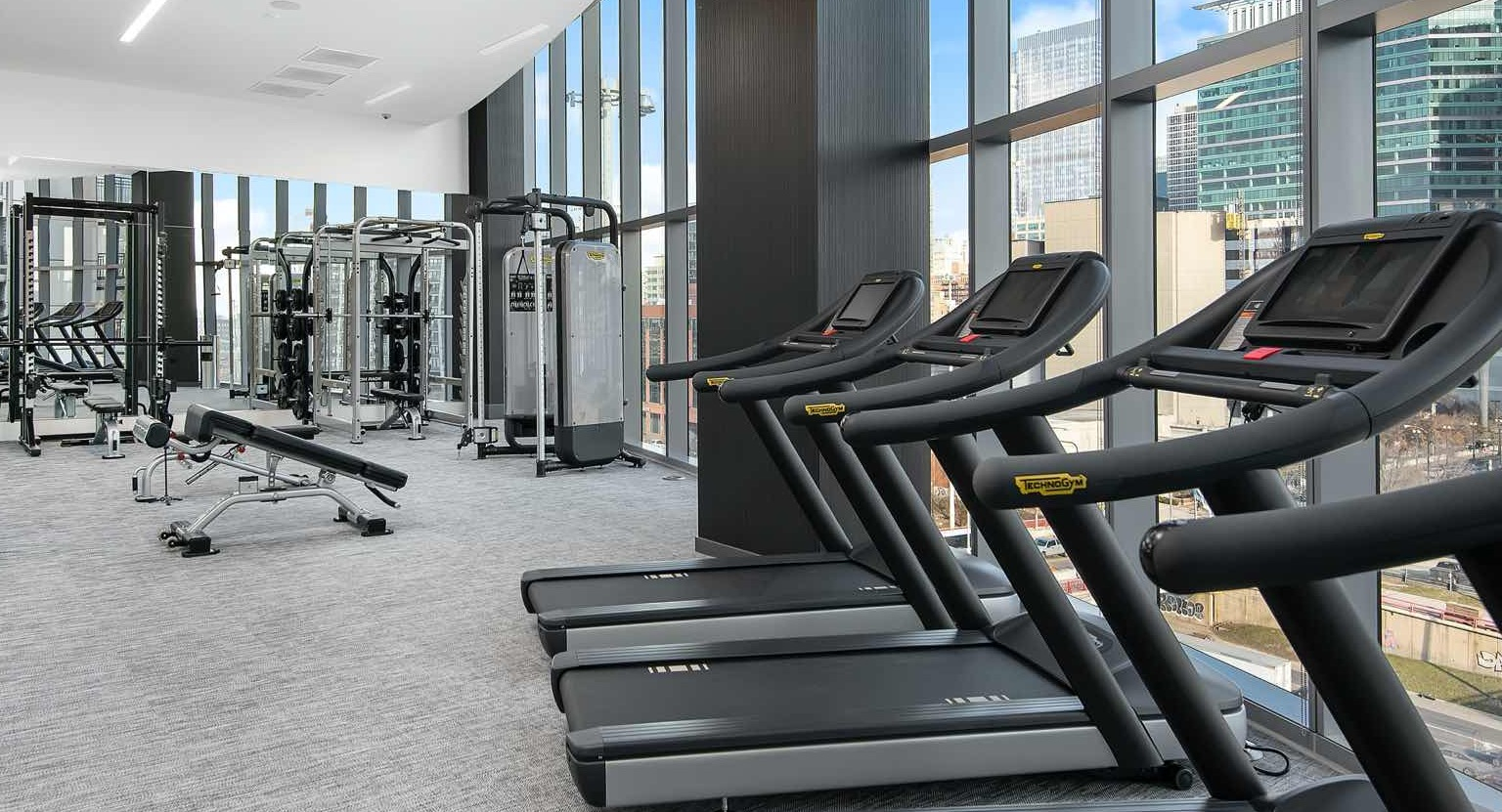 Light-filled fitness center at 727 West Madison in Chicago, with treadmills, strength equipment, and skyline views through tall windows