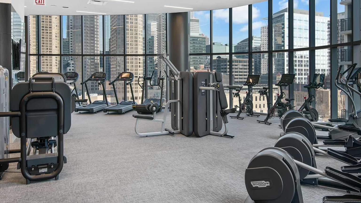 Expansive gym at 727 West Madison in Chicago with weight machines, ellipticals, and a row of spin bikes set before sweeping glass walls