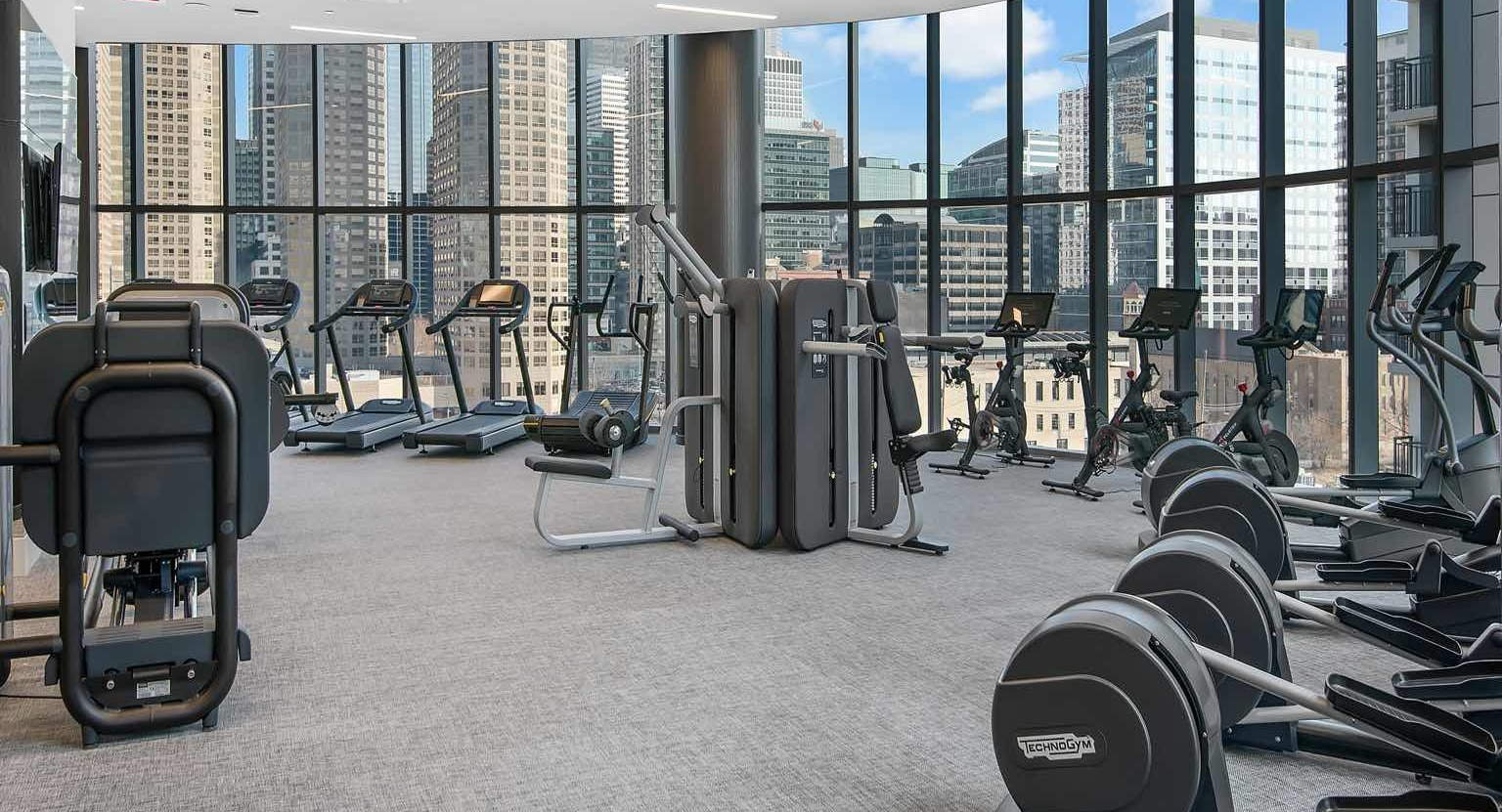 Expansive gym at 727 West Madison in Chicago with weight machines, ellipticals, and a row of spin bikes set before sweeping glass walls