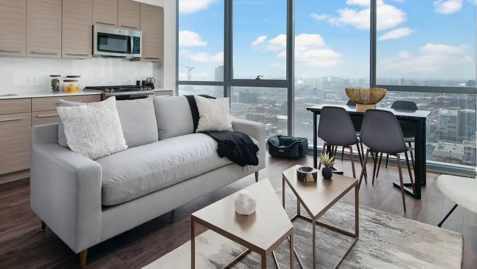 Modern living area with streamlined kitchen at 727 West Madison in Chicago, featuring a sofa, dining space, and full-height windows with city views