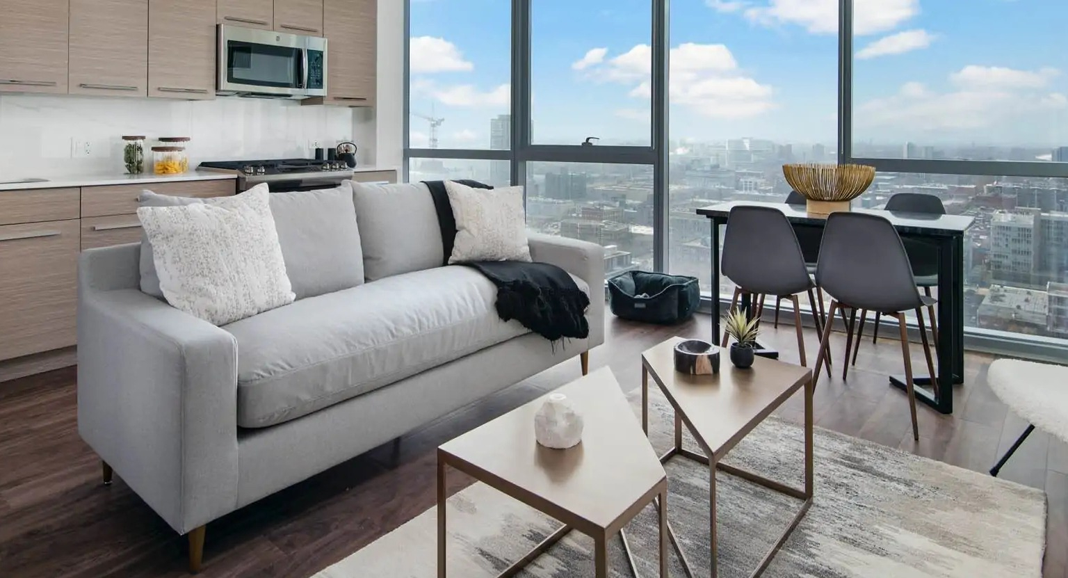 Modern living area with streamlined kitchen at 727 West Madison in Chicago, featuring a sofa, dining space, and full-height windows with city views