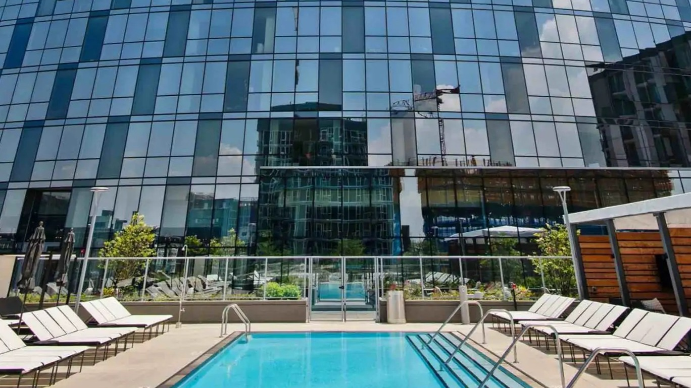 Sky-high facade framing the outdoor lap pool at 727 West Madison in Chicago, with lounge chairs and skyline reflections on the curved glass