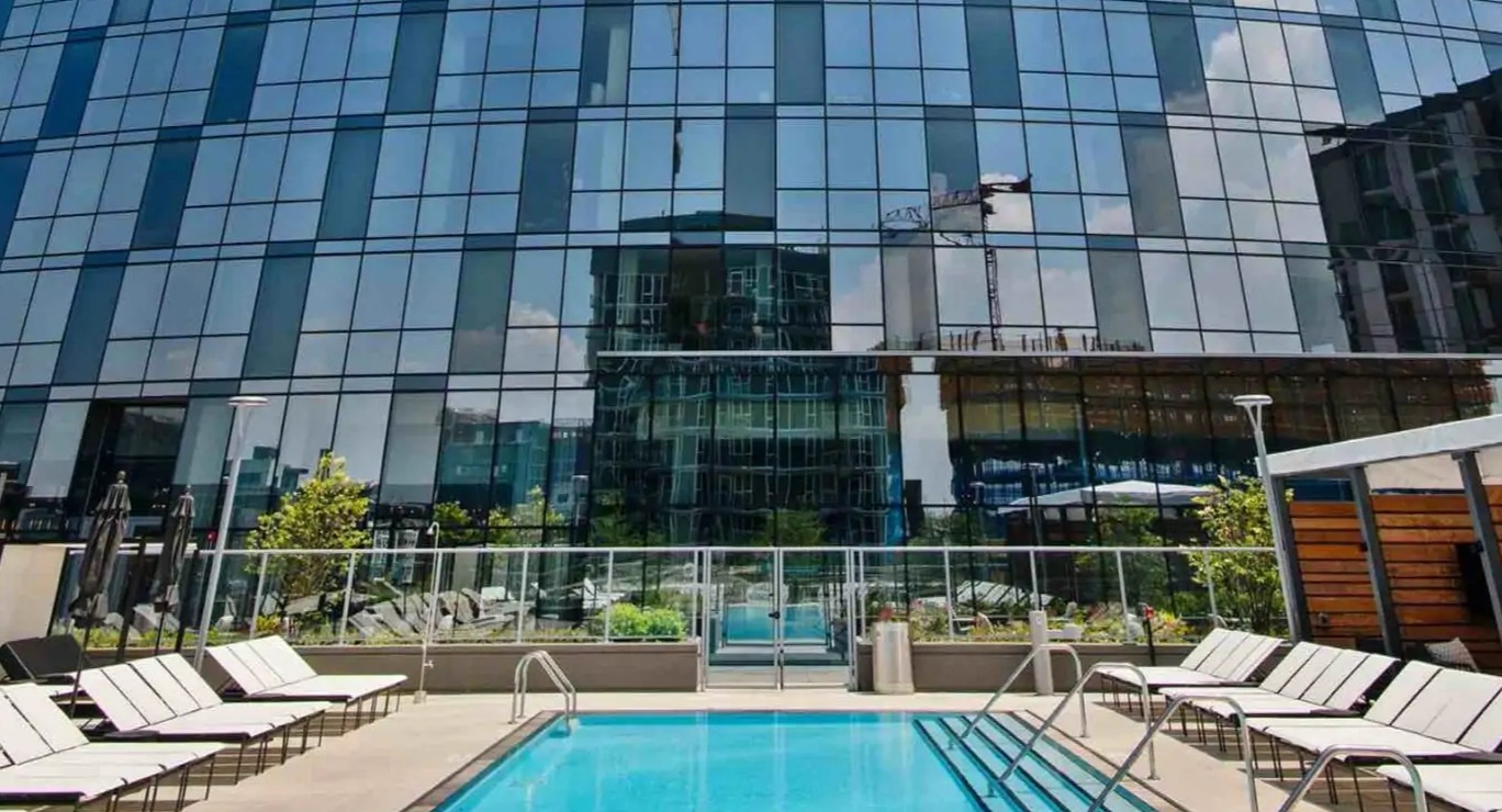 Sky-high facade framing the outdoor lap pool at 727 West Madison in Chicago, with lounge chairs and skyline reflections on the curved glass