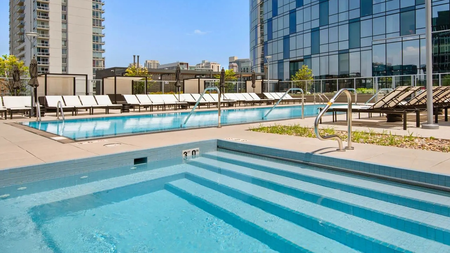 Outdoor pool and adjacent hot tub at 727 West Madison in Chicago, surrounded by chaise loungers, privacy screens, and skyline views