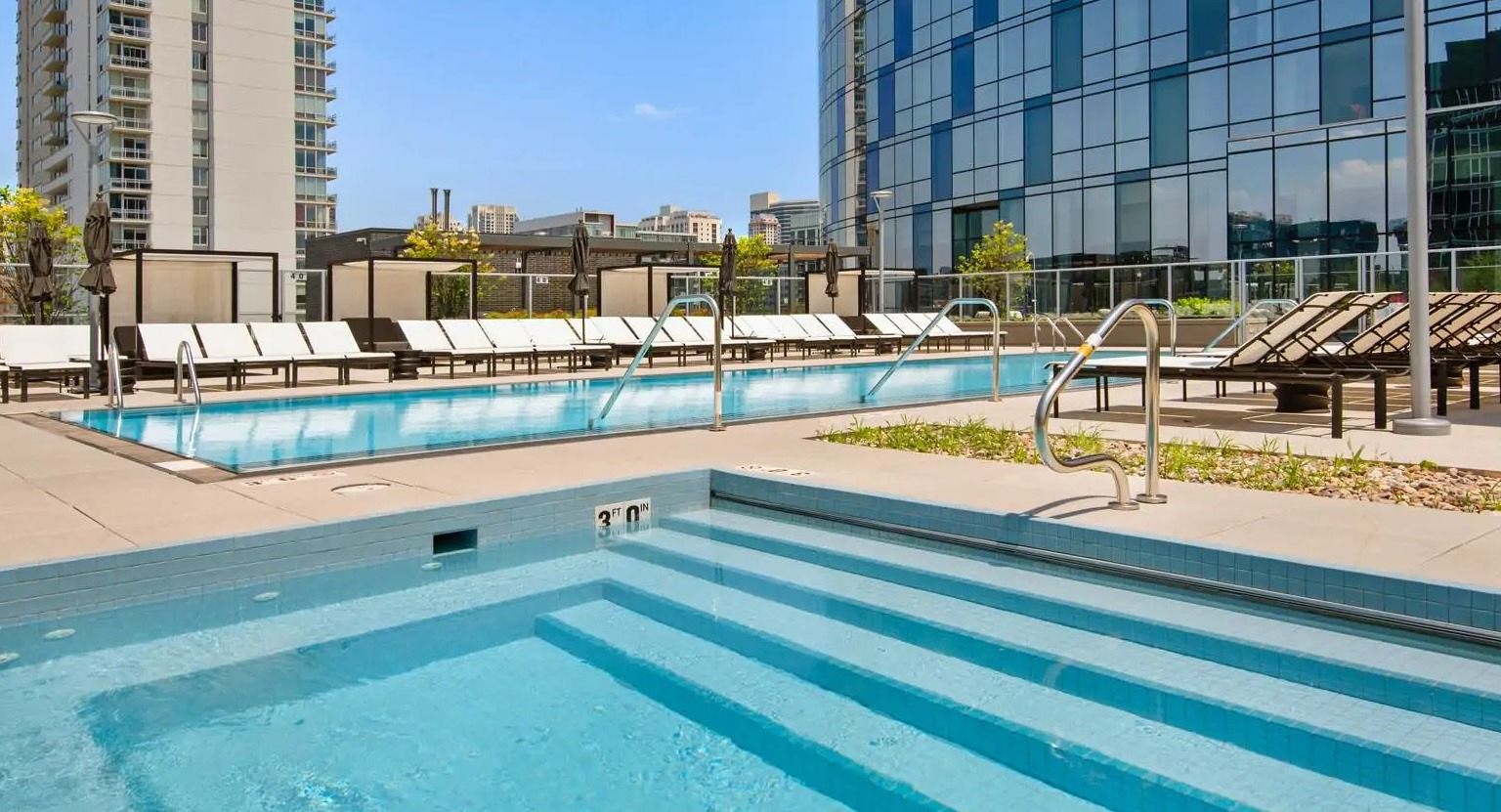 Outdoor pool and adjacent hot tub at 727 West Madison in Chicago, surrounded by chaise loungers, privacy screens, and skyline views