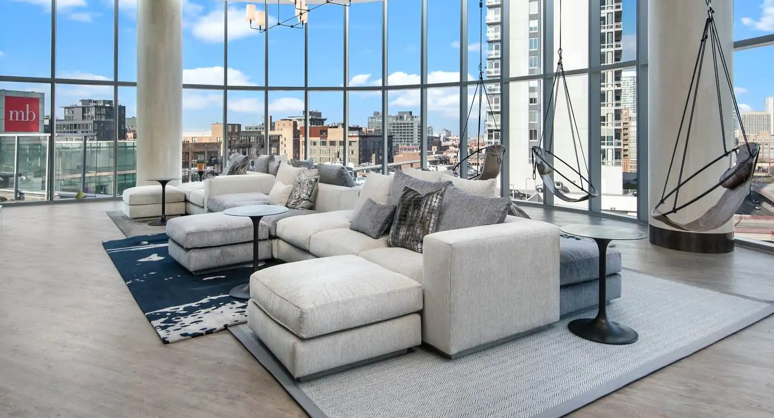 TV lounge at 727 West Madison in Chicago with sectional sofas, hanging swing chairs, floor-to-ceiling windows, and skyline views
