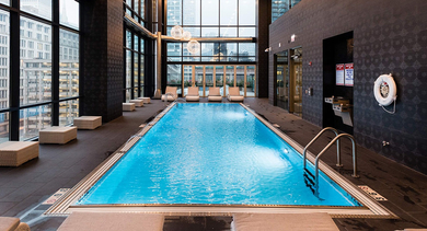 Indoor lap pool with tall windows, lounge seating, and modern lighting at 73 East Lake apartments in Chicago for year-round swimming