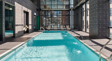 Indoor lap pool with floor-to-ceiling windows, water features, and lounge chairs at 73 East Lake apartments in Chicago
