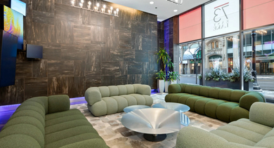 Contemporary lobby lounge with green modular sofas, chandelier lighting, and street-front windows at 73 East Lake apartments in Chicago