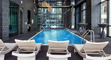Indoor pool area with white loungers, dramatic lighting, and soaring windows at 73 East Lake apartments in Chicago for relaxing pool days