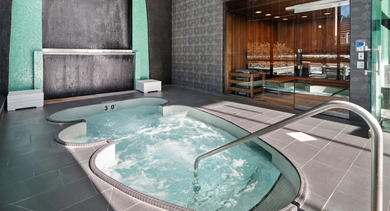Indoor spa with hot tub, dramatic water wall, and adjacent sauna at 73 East Lake apartments in Chicago