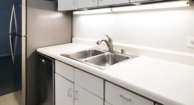 Bright white galley kitchen at 731 Plymouth in Chicago featuring plentiful cabinets, double sink, undercabinet lighting, and sleek solid-surface counters