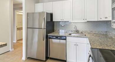 Bright kitchen at 750 N Rush St apartments in Chicago with white cabinets, granite counters, subway-tile backsplash, and stainless appliances
