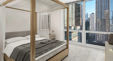 Cozy primary bedroom featuring a canopy bed, soft neutral finishes, and expansive city views at 750 N Rush St apartments in Chicago, perfect for restful urban living