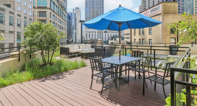 Sunny dining terrace at 750 N Rush St apartments in Chicago with table seating, blue umbrellas, greenery, and skyline views for relaxed outdoor meals