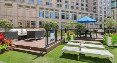 Rooftop-style lounge at 750 N Rush St in Chicago featuring sun loungers on turf, seating areas, planters, and umbrellas amid downtown buildings