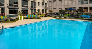 Rooftop pool with lounge chairs, landscaping, and city high-rise backdrop at 750 N Rush St apartments in Chicago, offering a sunny sundeck for relaxing and swimming
