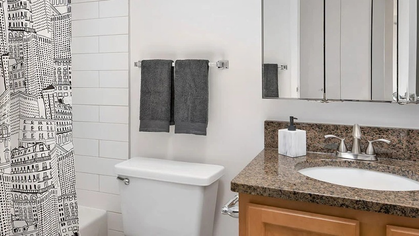 Updated bathroom with granite vanity, subway-tile tub, and a playful cityscape shower curtain at 777 South State apartments in Chicago