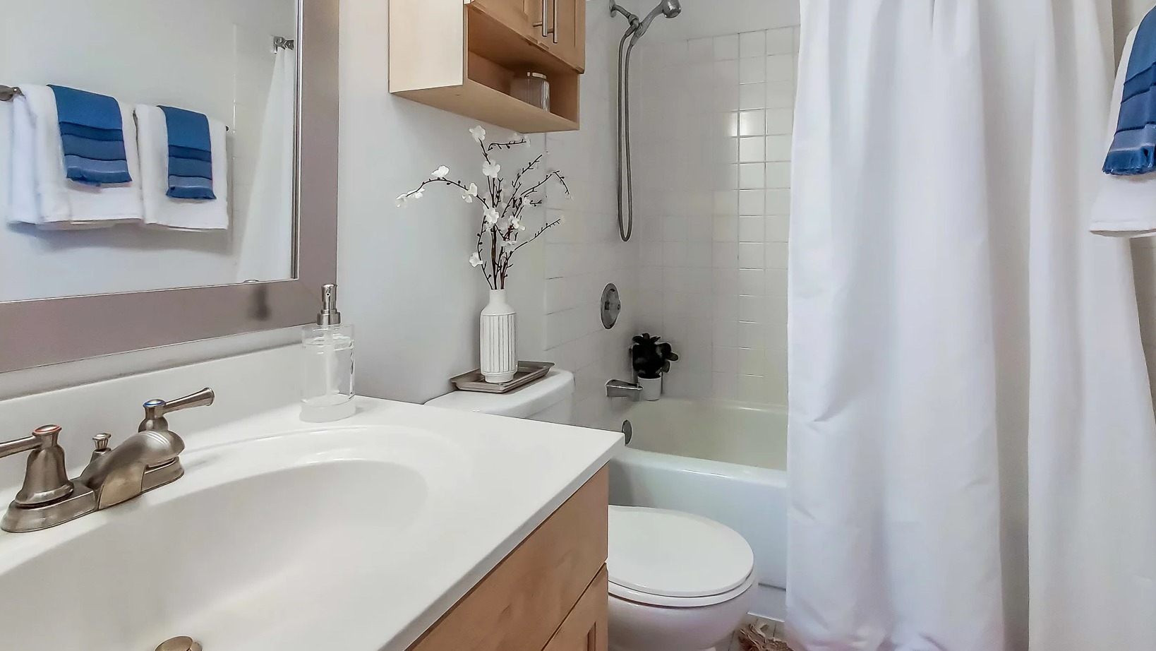 Bright bathroom with light wood vanity, wide mirror, white tile tub, and shower curtain at 777 South State apartments in Chicago
