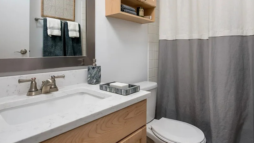 Renovated bathroom with light wood vanity, quartz counter, and two-tone shower curtain at 777 South State apartments in Chicago
