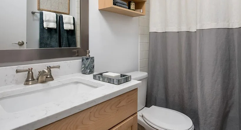 Renovated bathroom with light wood vanity, quartz counter, and two-tone shower curtain at 777 South State apartments in Chicago