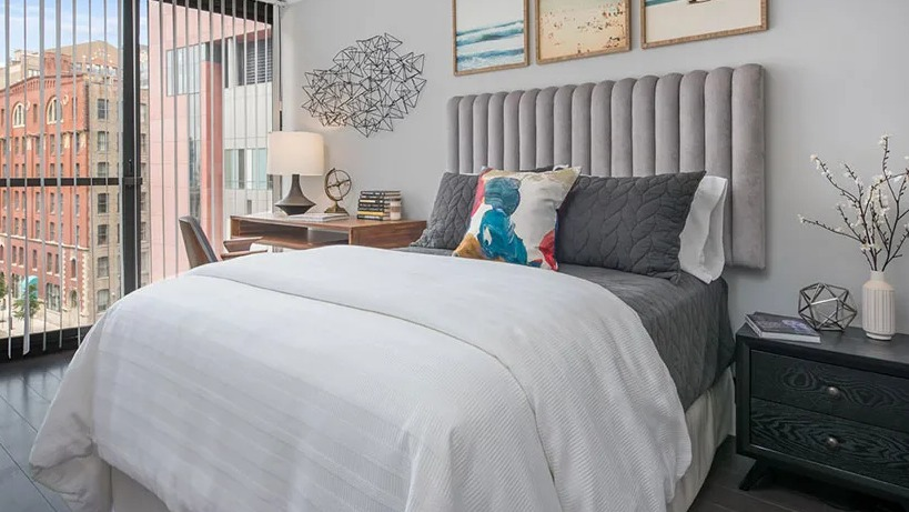 Sunny bedroom with plush channel-tufted headboard, desk by the window, and city views at 777 South State apartments in Chicago