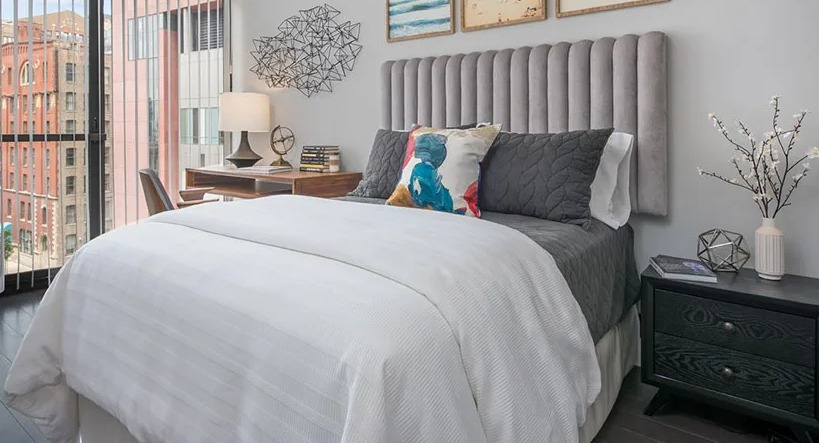 Sunny bedroom with plush channel-tufted headboard, desk by the window, and city views at 777 South State apartments in Chicago
