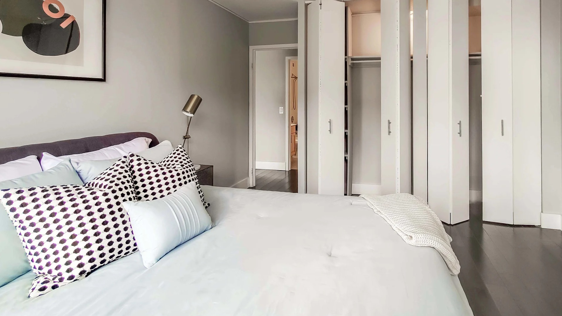 Cozy bedroom with neutral walls, upholstered bed, accent pillows, and a wall of closets at 777 South State apartments in Chicago