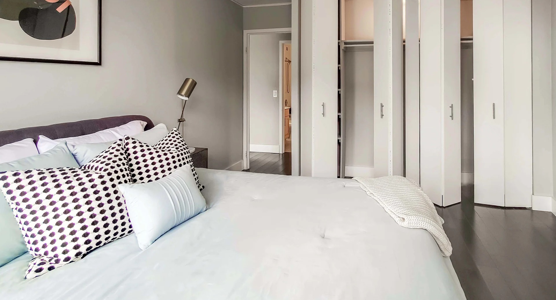 Cozy bedroom with neutral walls, upholstered bed, accent pillows, and a wall of closets at 777 South State apartments in Chicago
