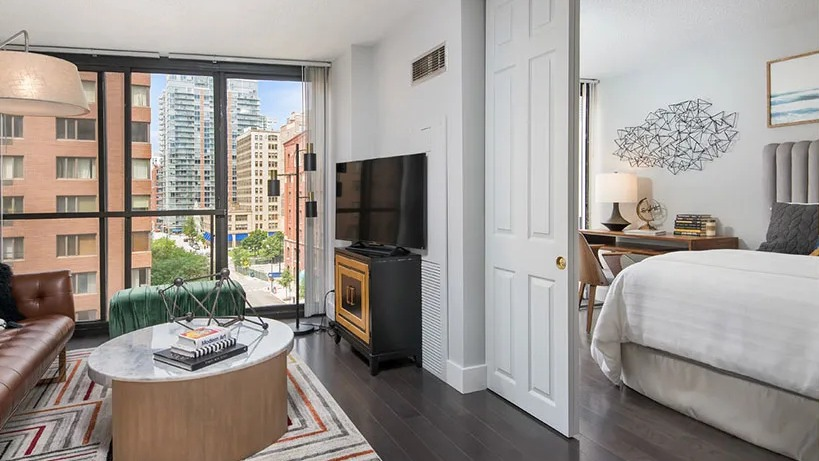 Chic den and bedroom suite with brown leather sofa, sliding doors, and city views at 777 South State apartments in Chicago